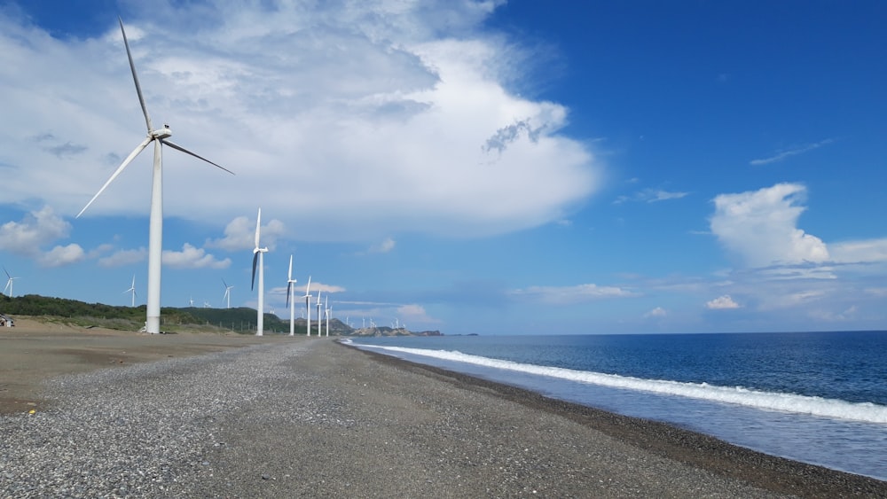 a row of wind turbines next to the ocean
