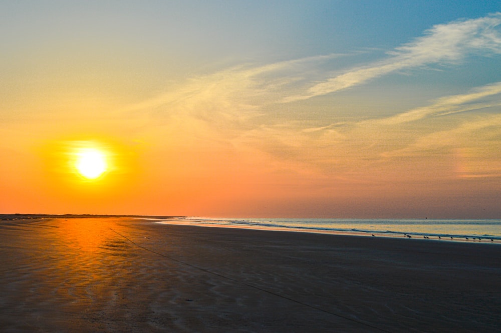 the sun is setting on the beach with the ocean in the background