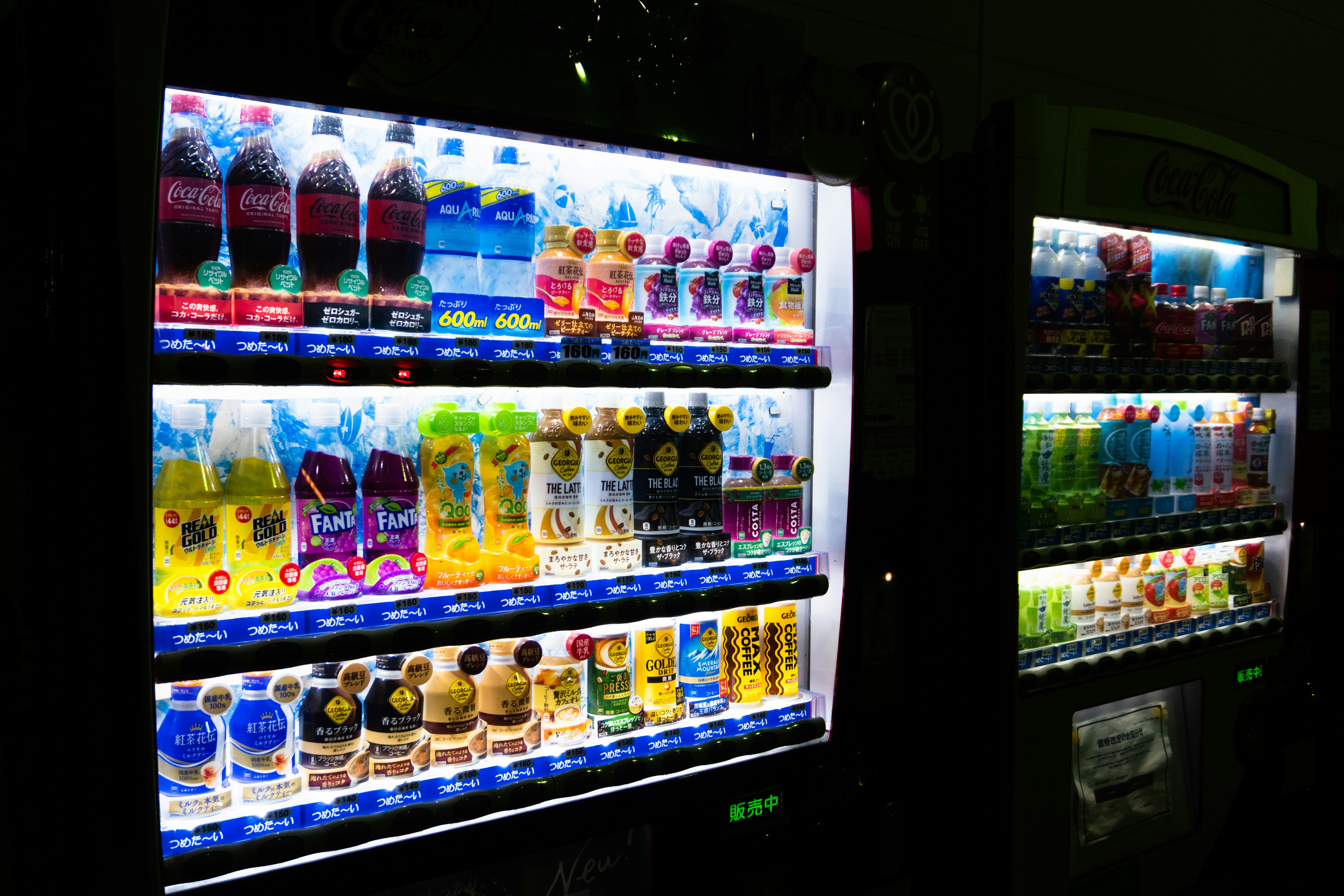 Illuminated beverage vending machine with rows of colorful drinks in modern lobby at dusk