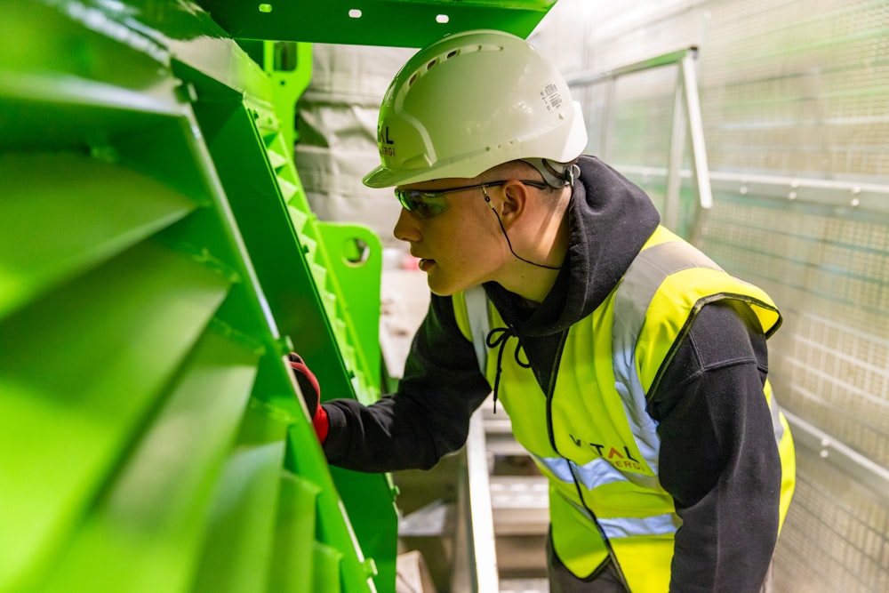 a man in a hard hat and safety vest working on a green structure