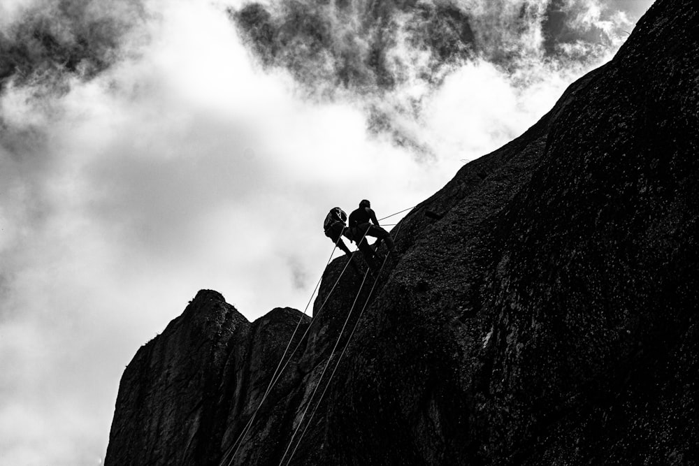 two people climbing up the side of a mountain