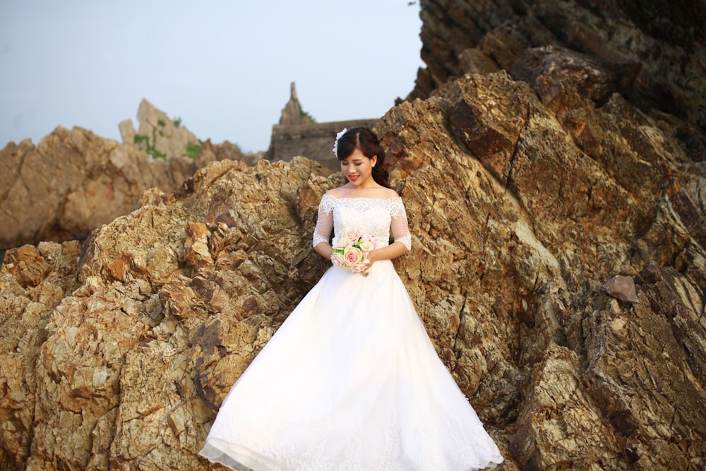 a woman in a wedding dress standing on rocks