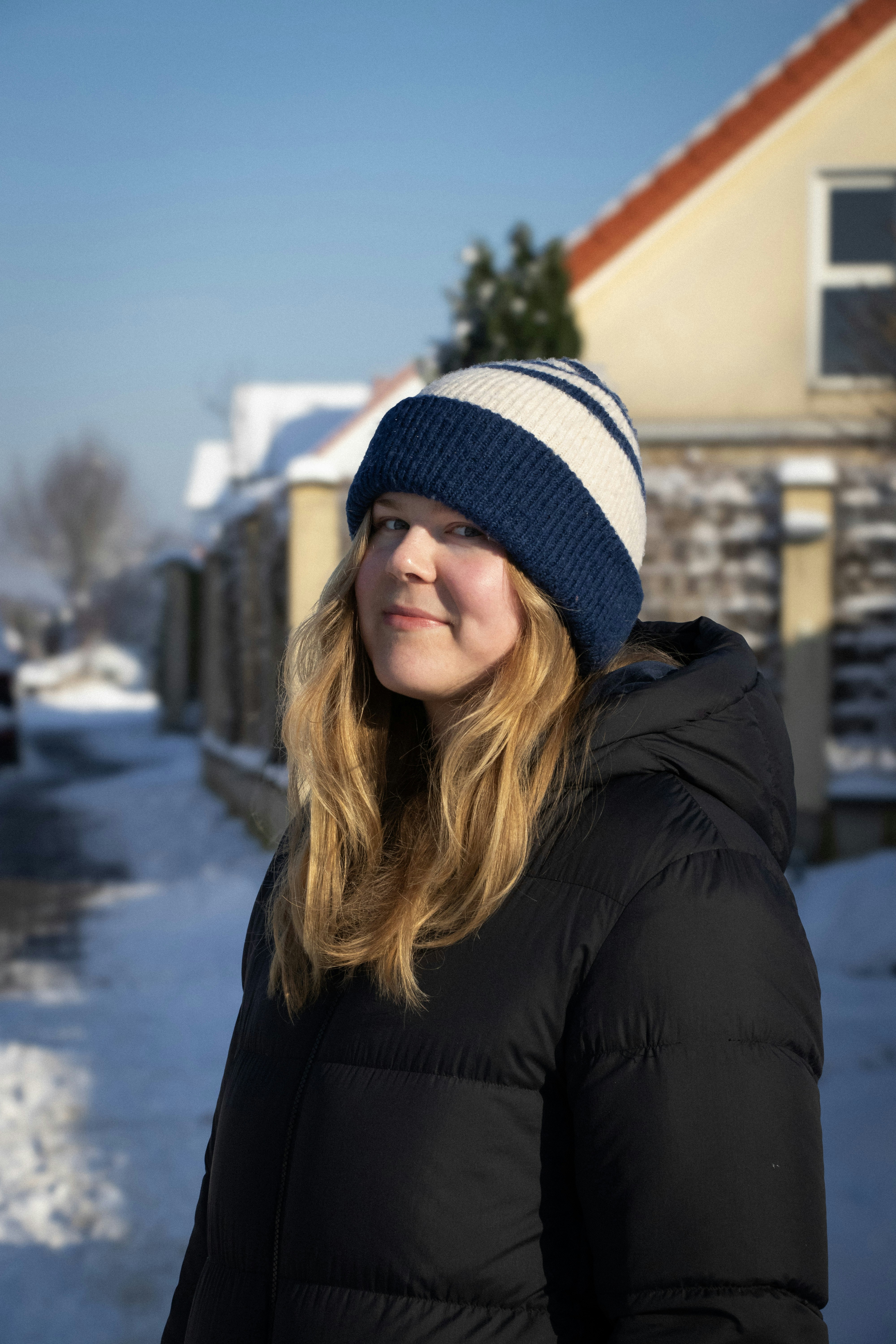 una mujer parada en la nieve frente a una casa
