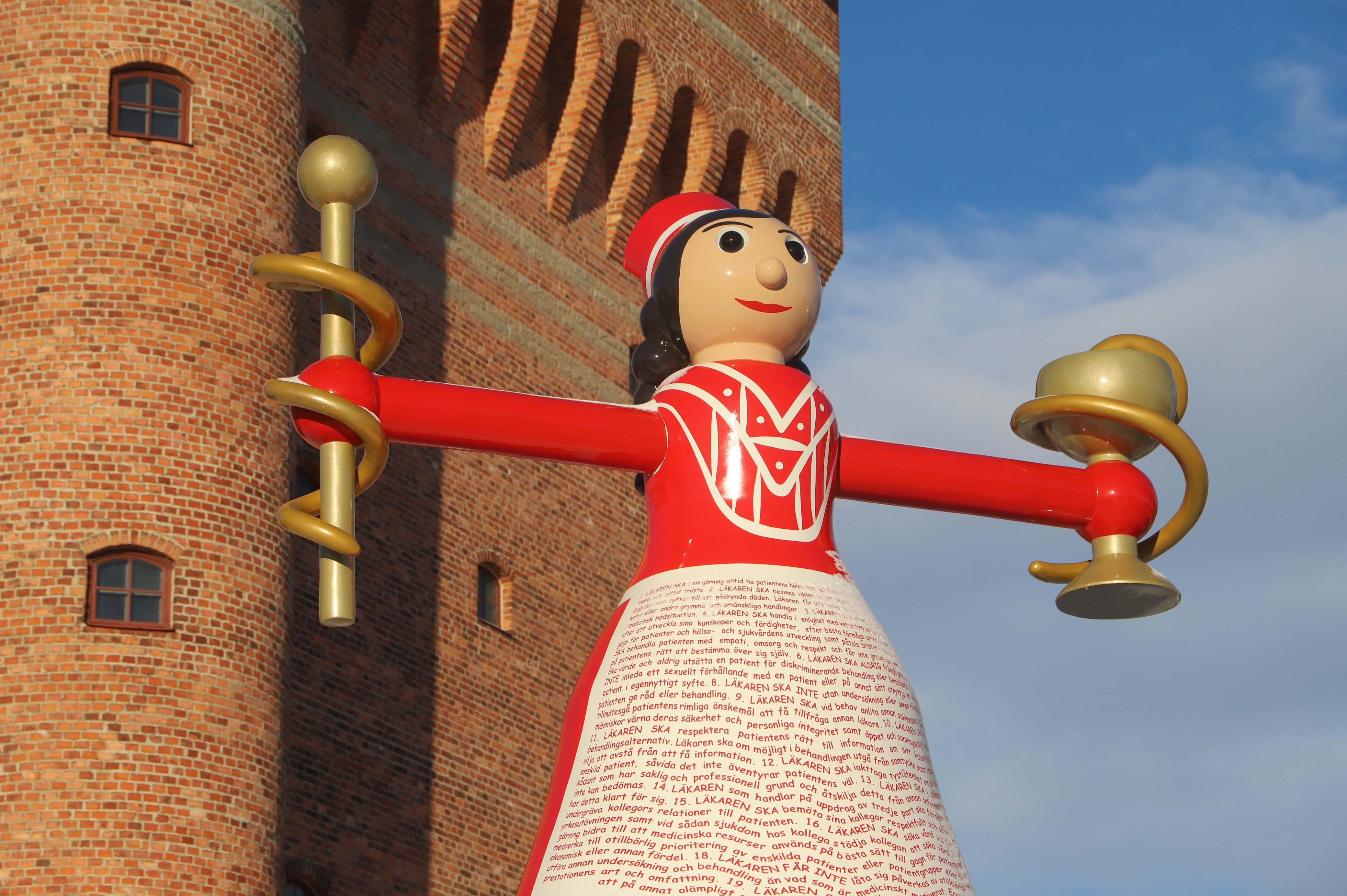 a statue of a woman holding a bell in front of a brick building
