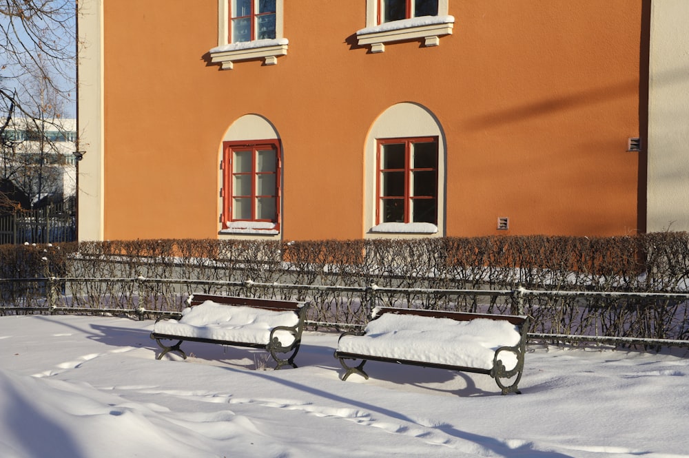 two benches covered in snow in front of a building