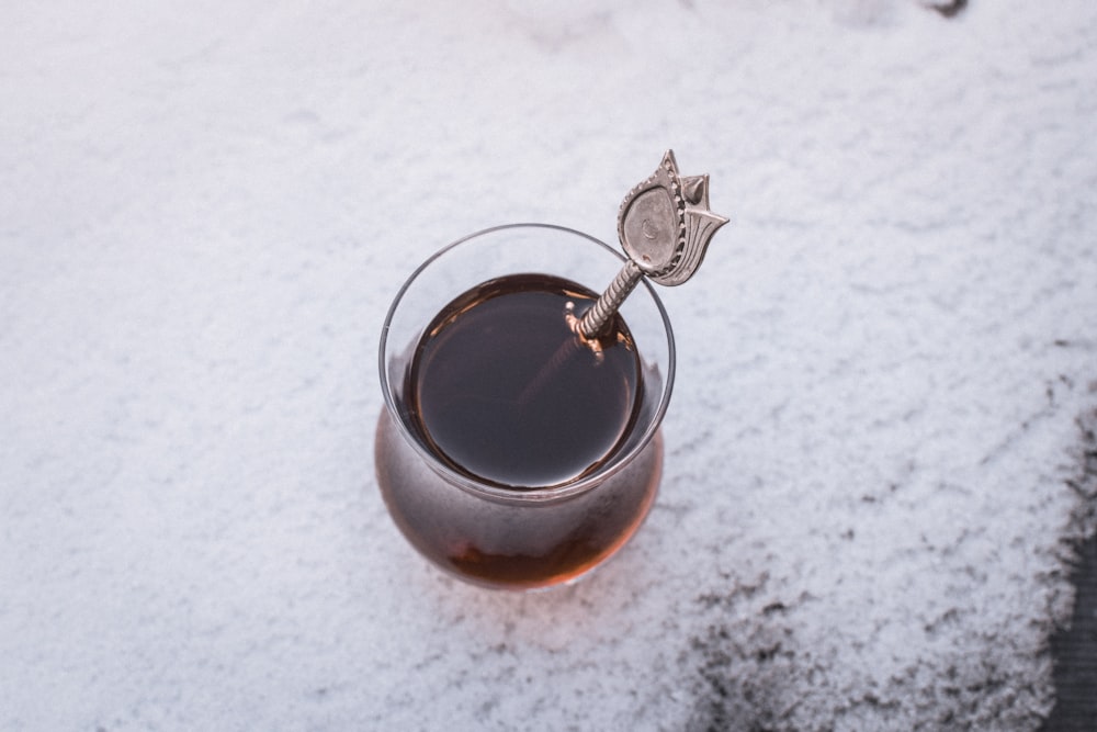 a glass filled with liquid sitting on top of a snow covered ground