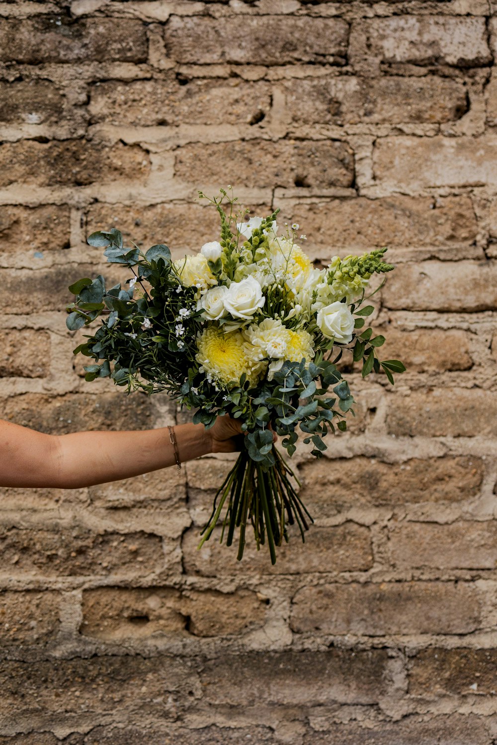 a woman holding a bouquet of flowers in front of a brick wall