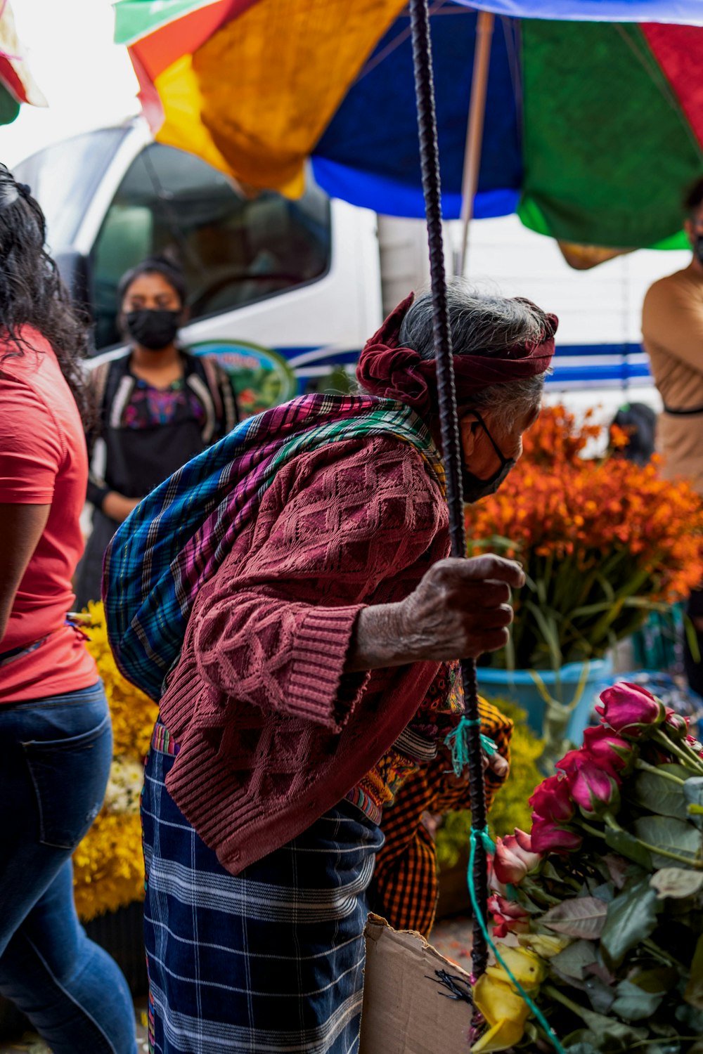 a woman standing under an umbrella next to a bunch of flowers