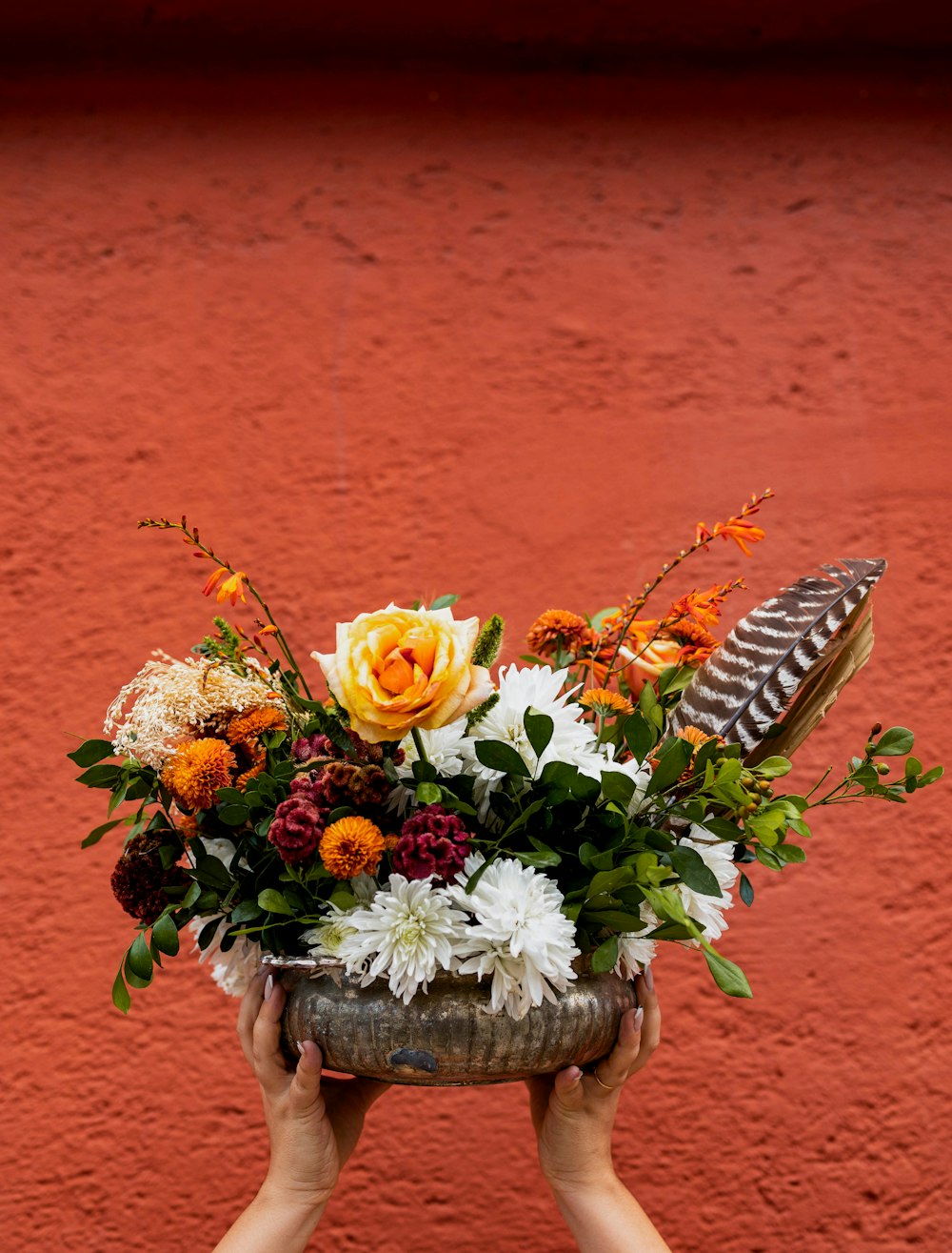 a person holding a flower arrangement in front of a red wall