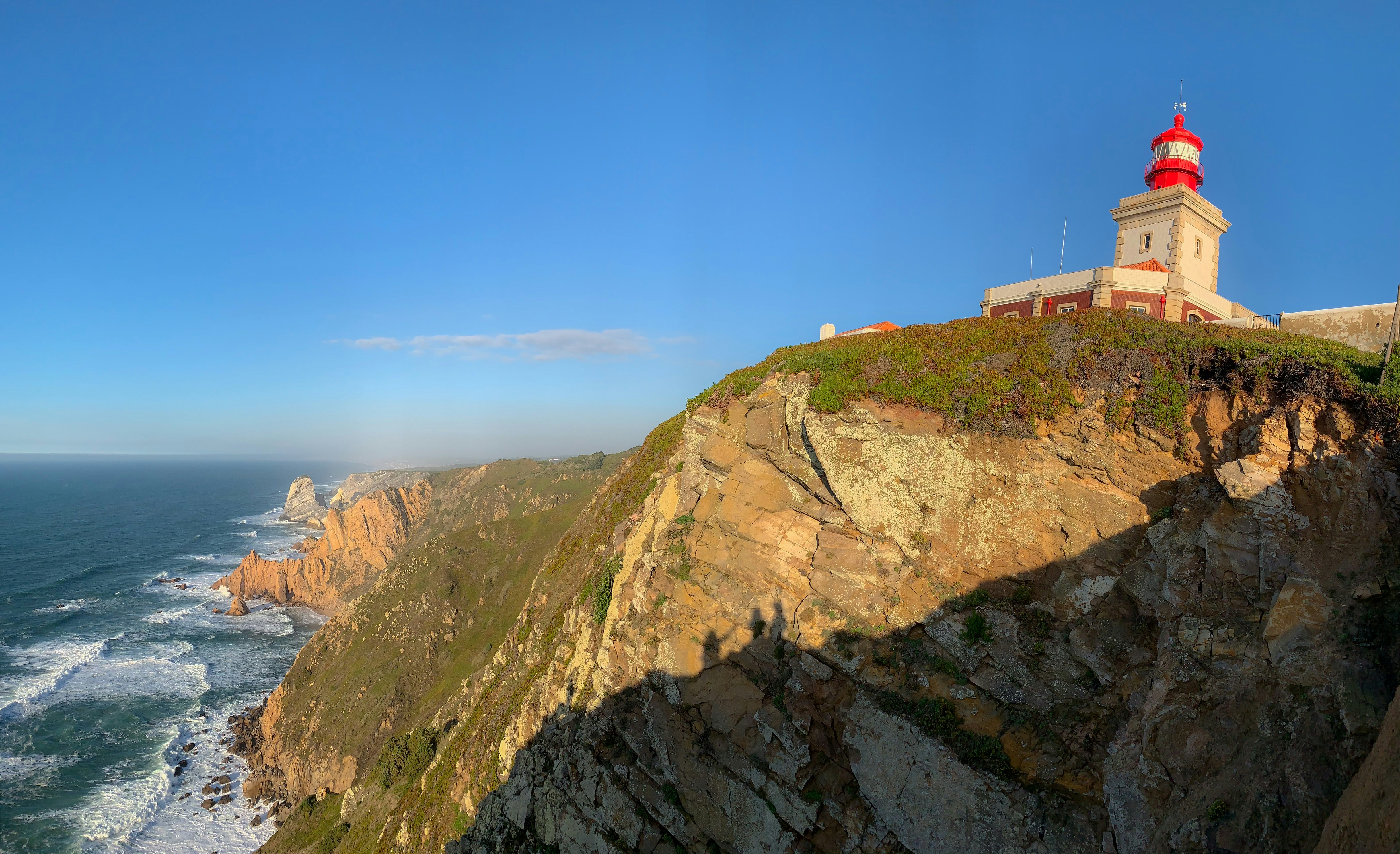 a lighthouse on a cliff overlooking the ocean, The red-capped lighthouse atop rugged cliffs against the vast ocean at Cabo da Roca