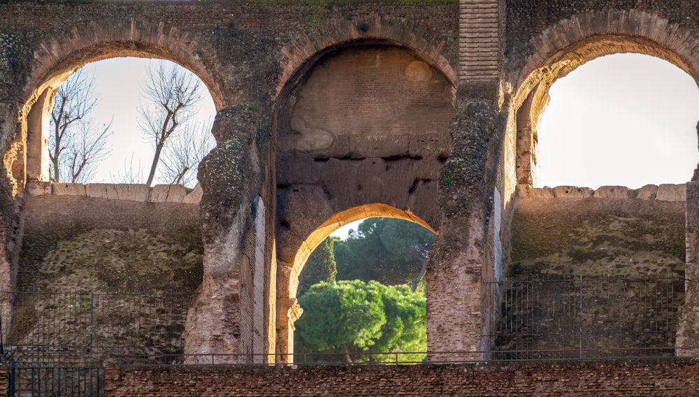 a stone wall with arches and trees in the background