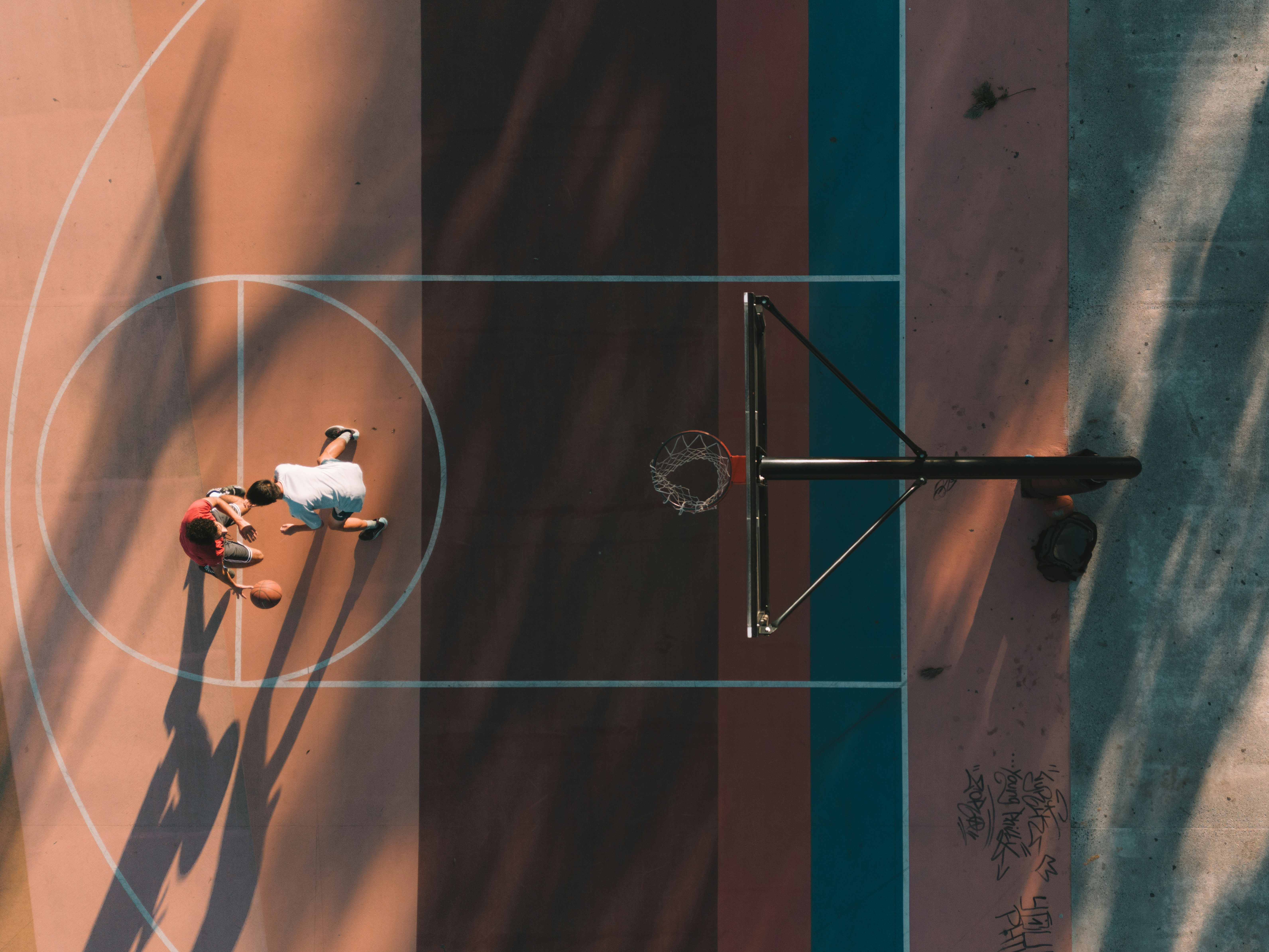 A bird's-eye view of players engaged in a basketball game, casting long shadows on the vibrant, multicolored court below.