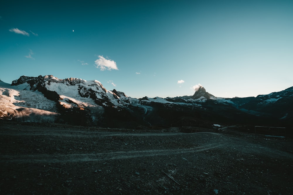 a dirt road in front of a snow covered mountain