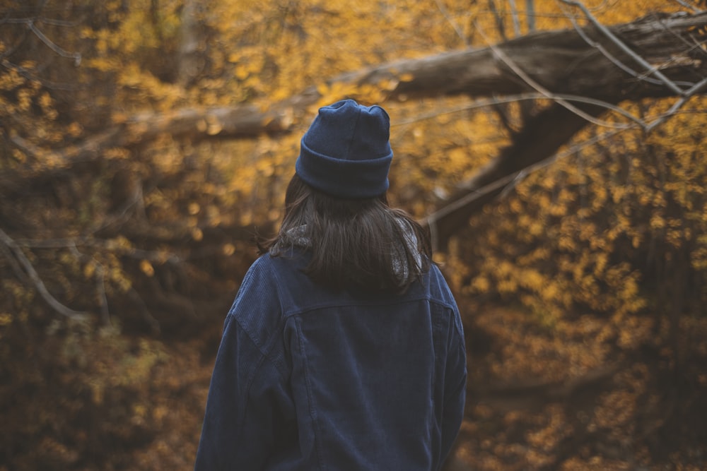 a person in a blue jacket and hat walking through a forest