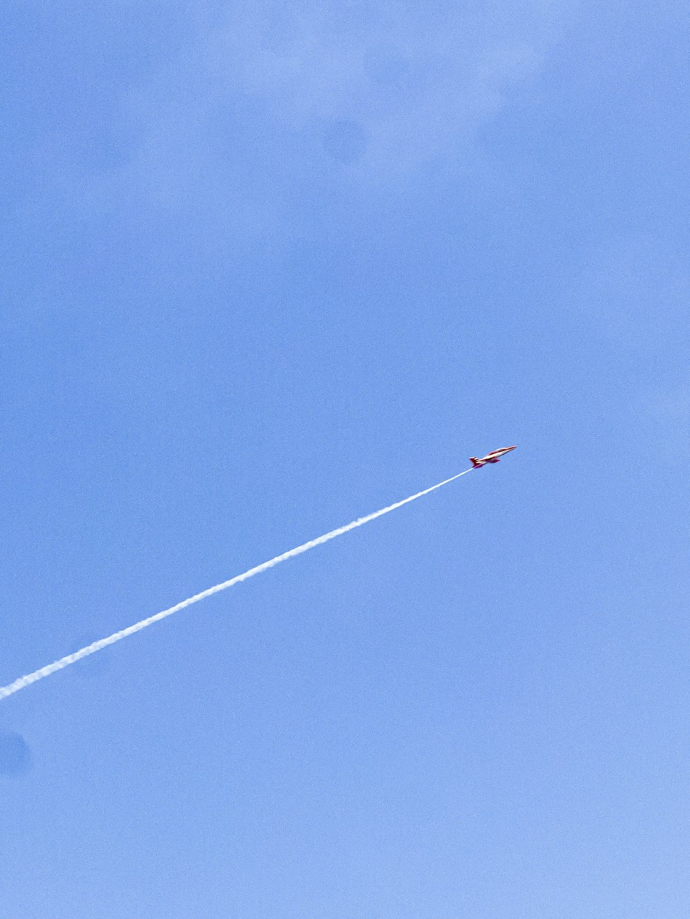 ein Flugzeug, das mit einem Kondensstreifen im Rücken am Himmel fliegt