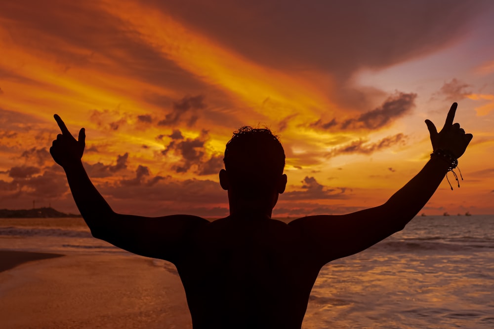 a man standing on a beach holding his hands up in the air