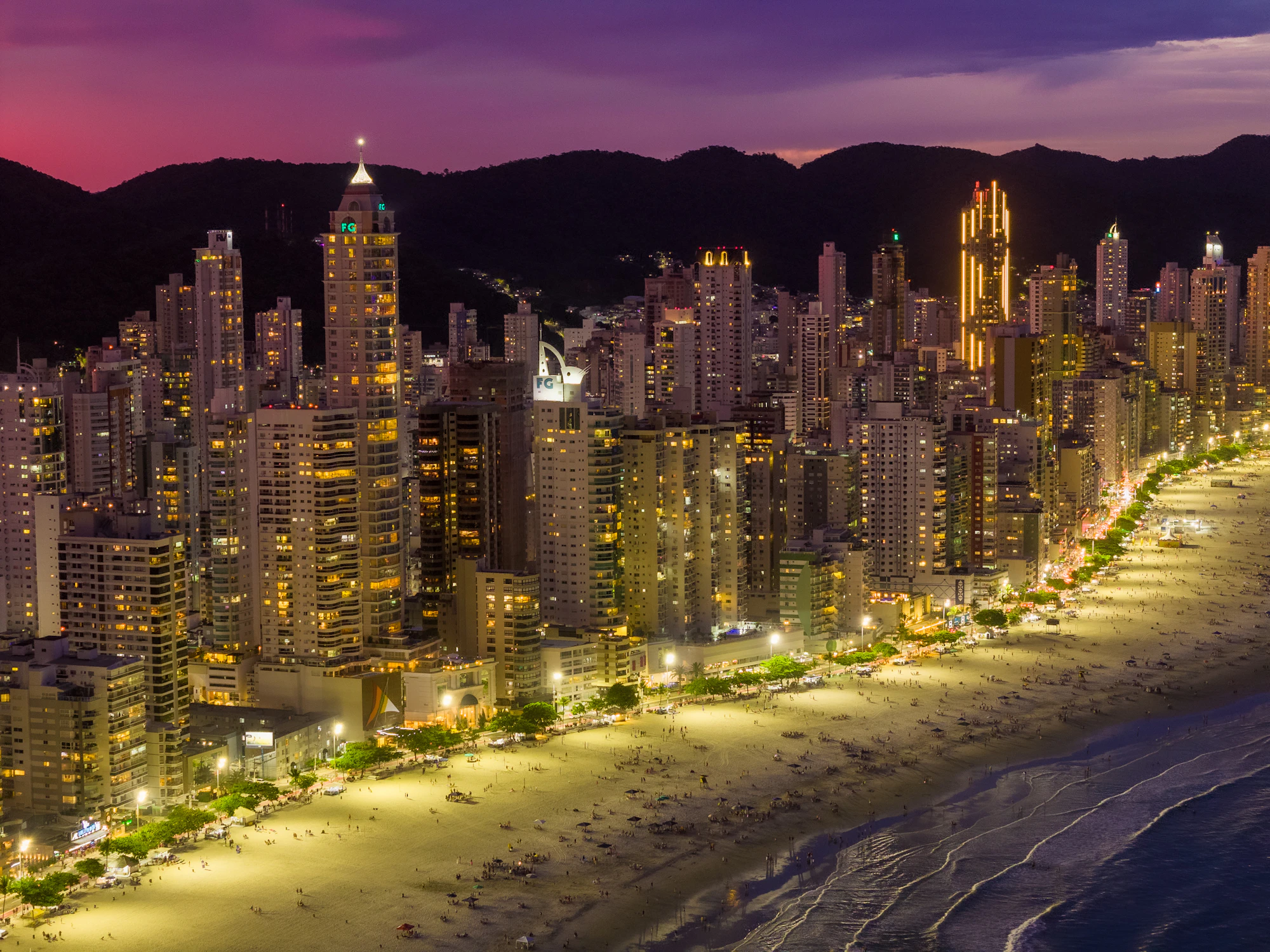 Litoral catarinense ao anoitecer, com praia e cidade iluminada