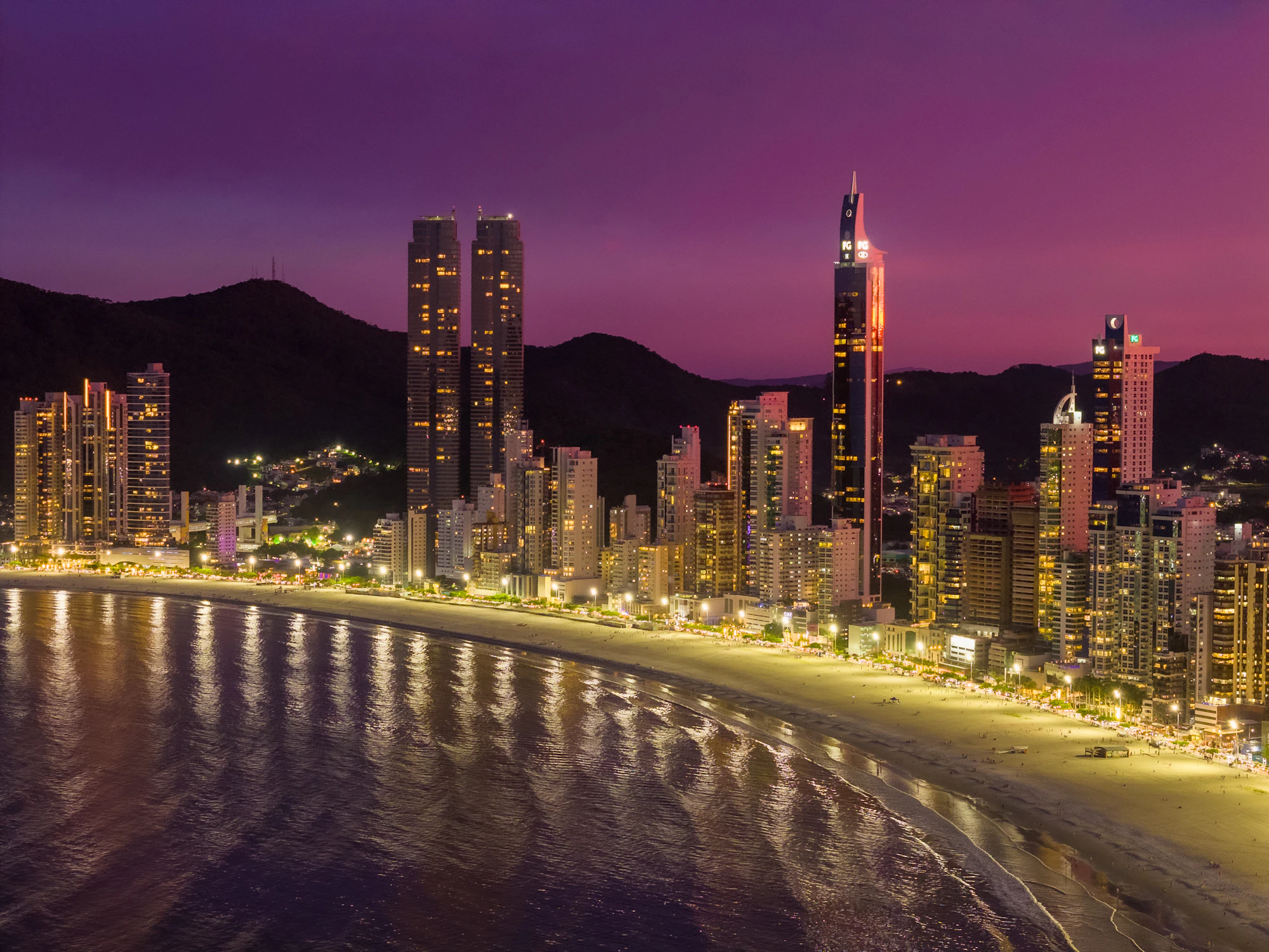 Skyline do litoral catarinense ao anoitecer, entre praia e montanhas