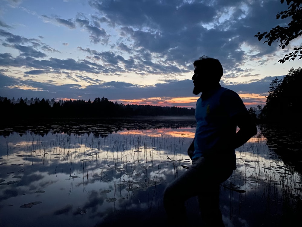 a man standing in front of a lake at sunset