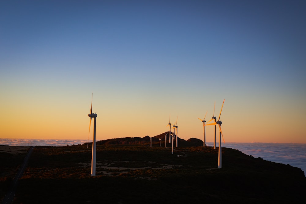 a group of windmills on a hill at sunset