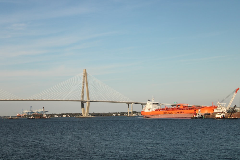 a large orange boat in the water near a bridge