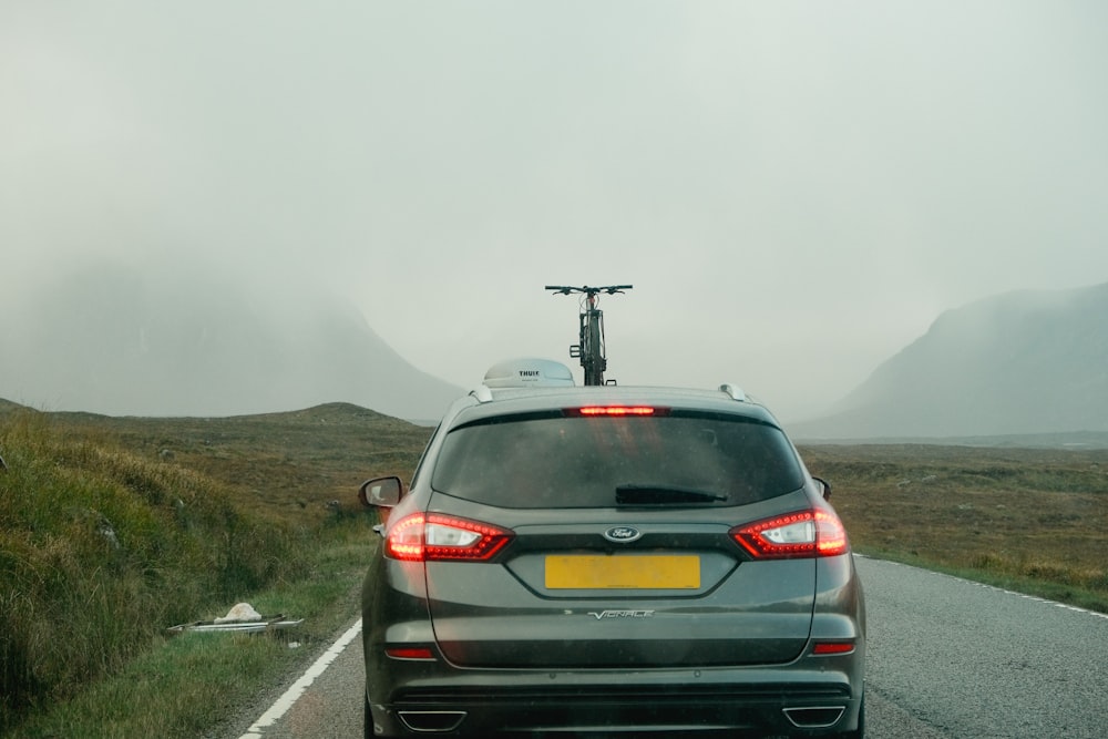 a car driving down a road with a bicycle on top of it
