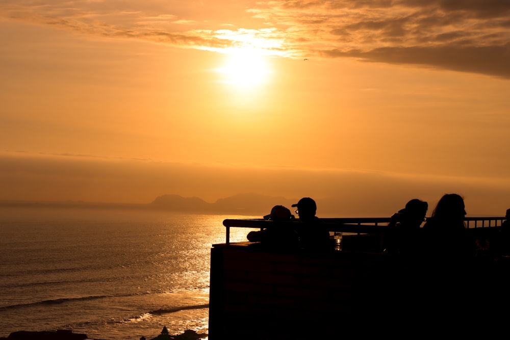 a group of people sitting on top of a bench near the ocean