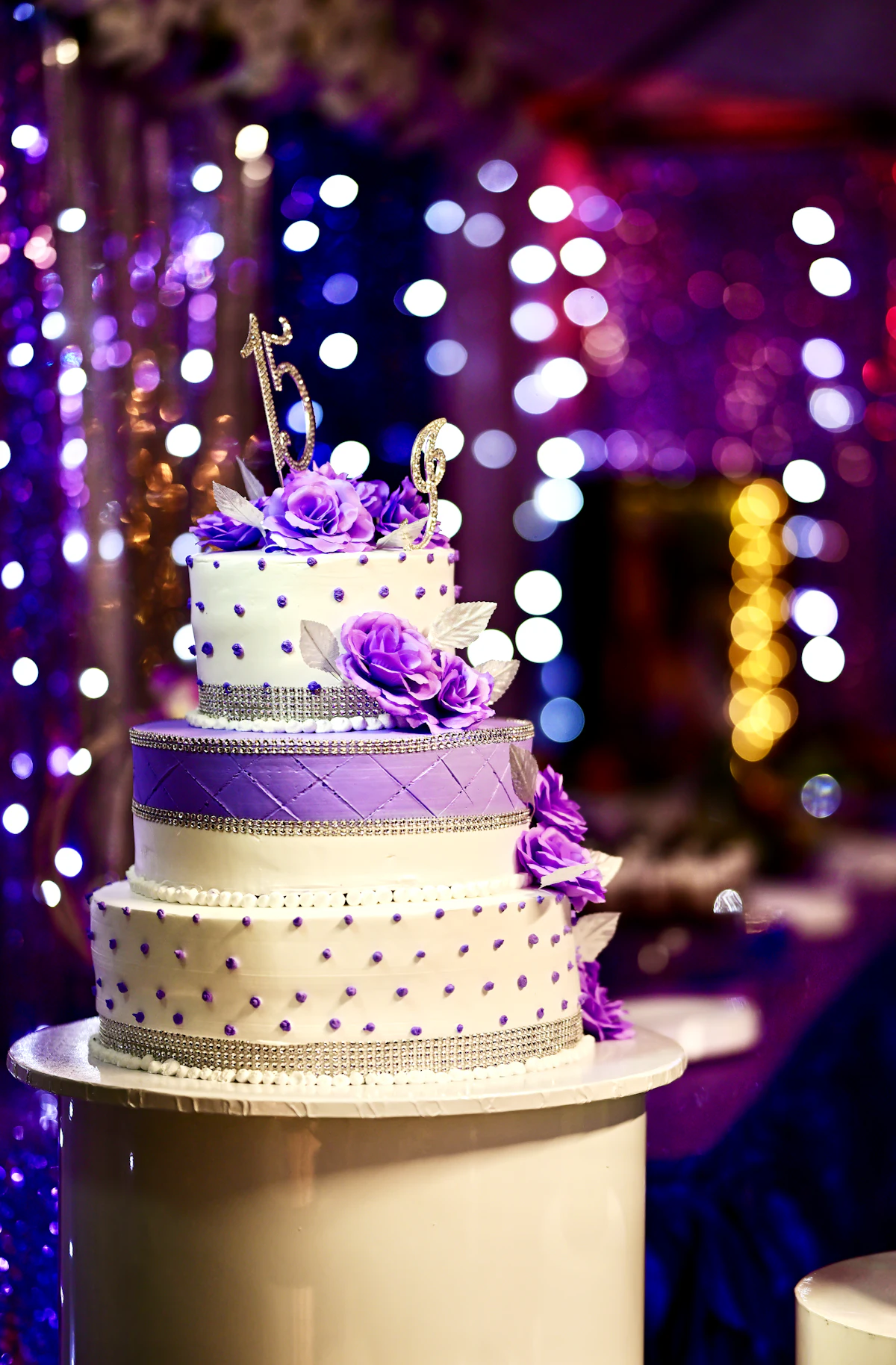 Torta de varios pisos con flores violetas y luces de fondo