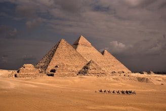 a group of people riding camels in front of three pyramids