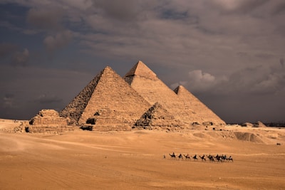 a group of people riding camels in front of three pyramids