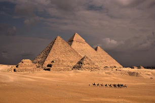 a group of people riding camels in front of three pyramids