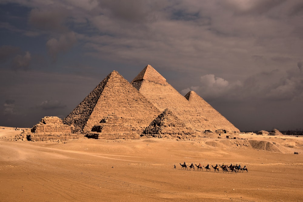 a group of people riding camels in front of three pyramids