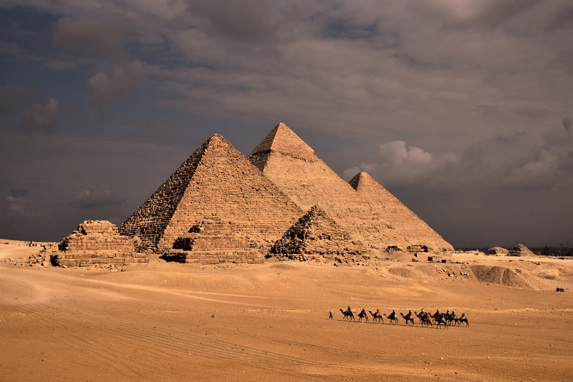 a group of people riding camels in front of three pyramids
