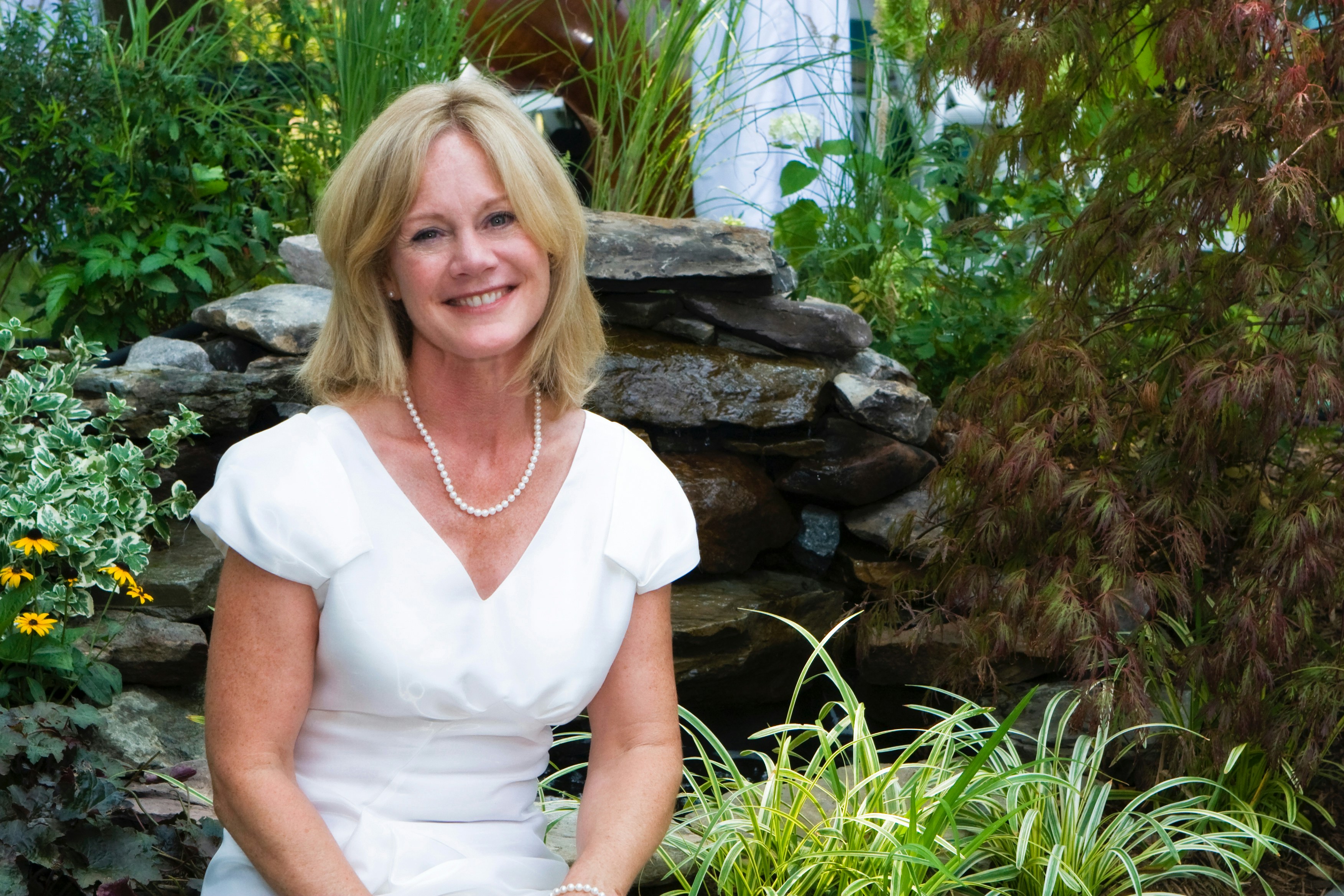 Elegant woman in white flowing dress, bright outdoor garden, sunlit