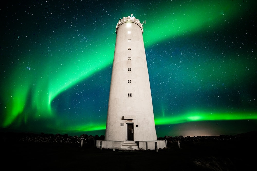a white lighthouse with a green aurora behind it