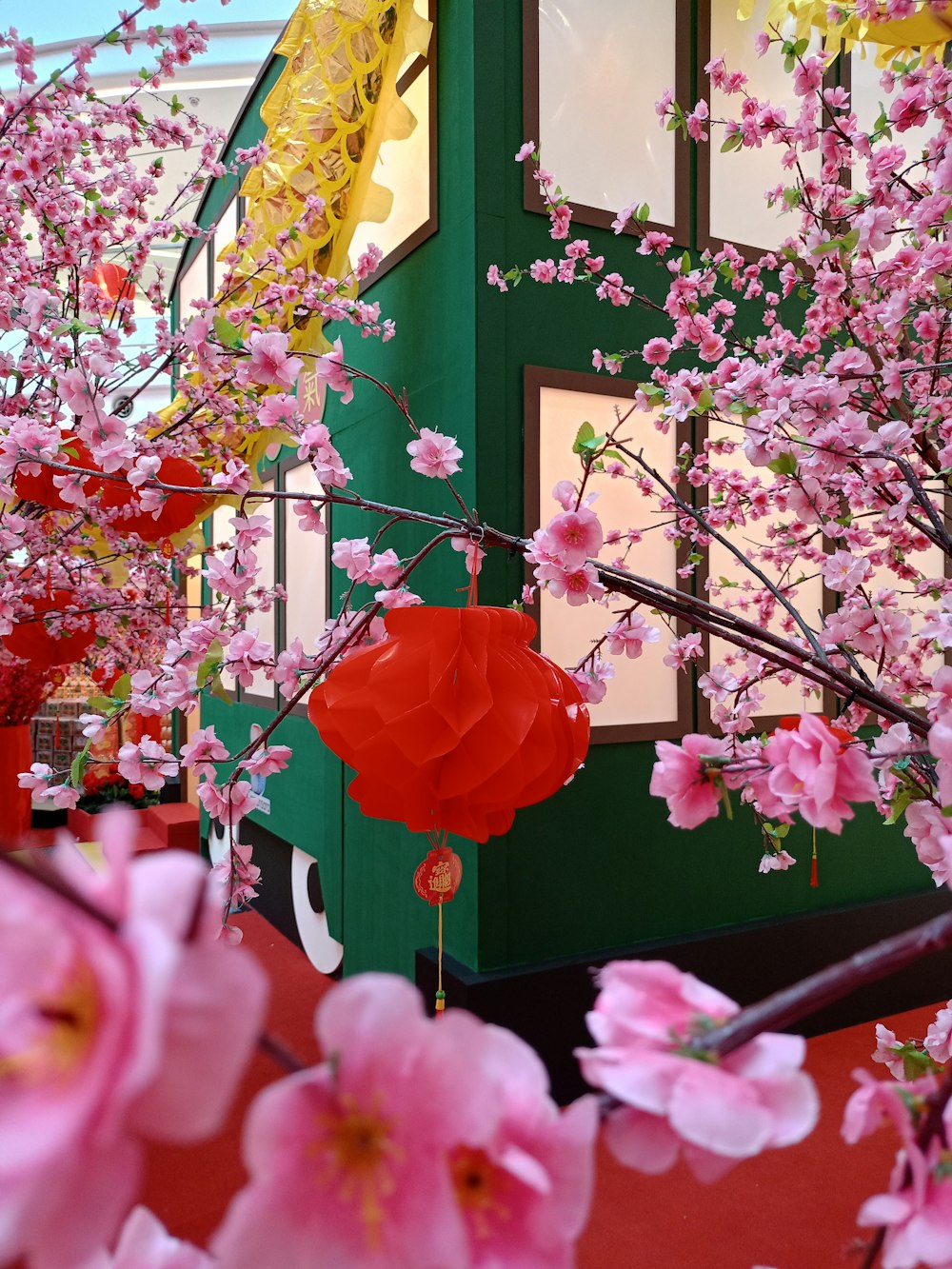 una lanterna di carta rossa appesa a un albero pieno di fiori rosa