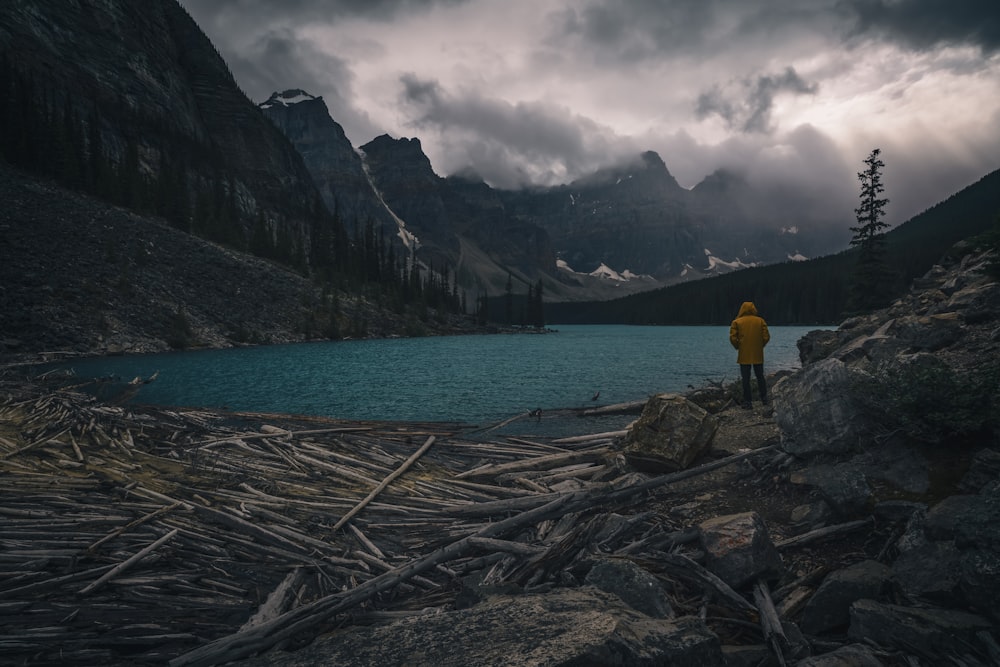 a person in a yellow jacket standing on rocks near a body of water