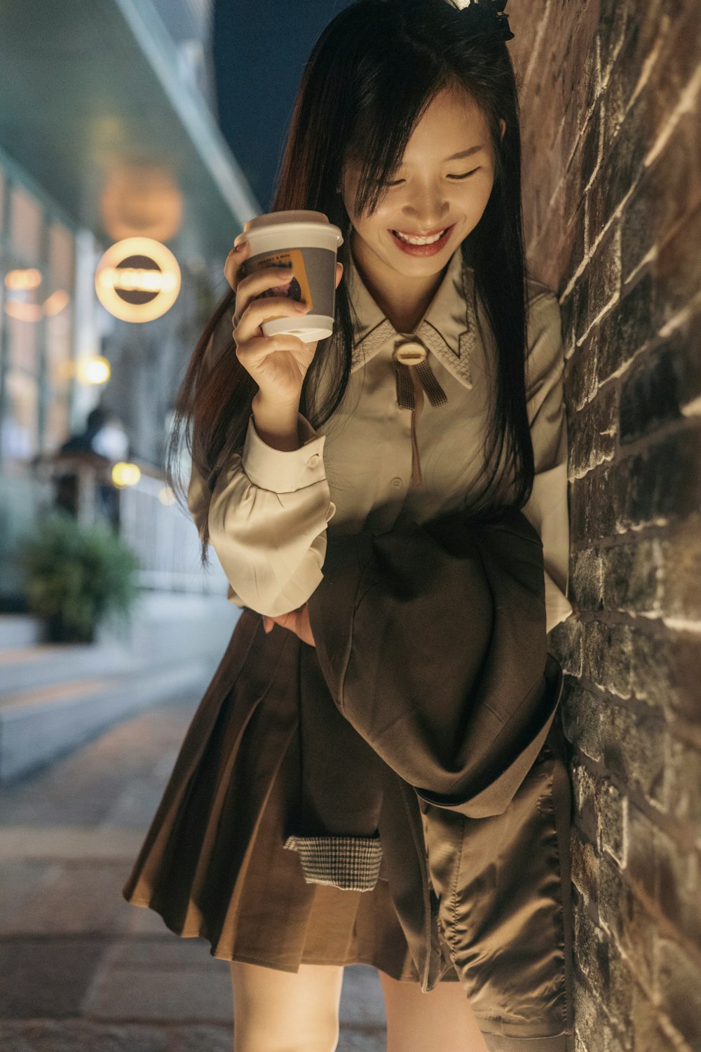 a woman holding a cup of coffee standing next to a brick wall