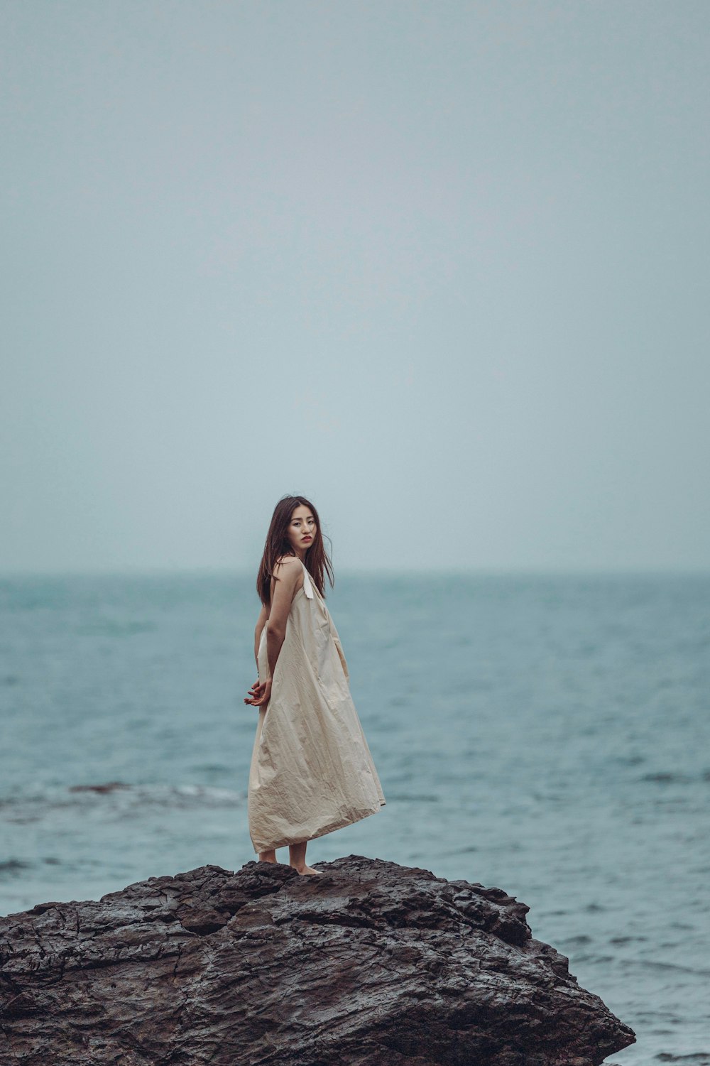 a woman standing on top of a rock near the ocean