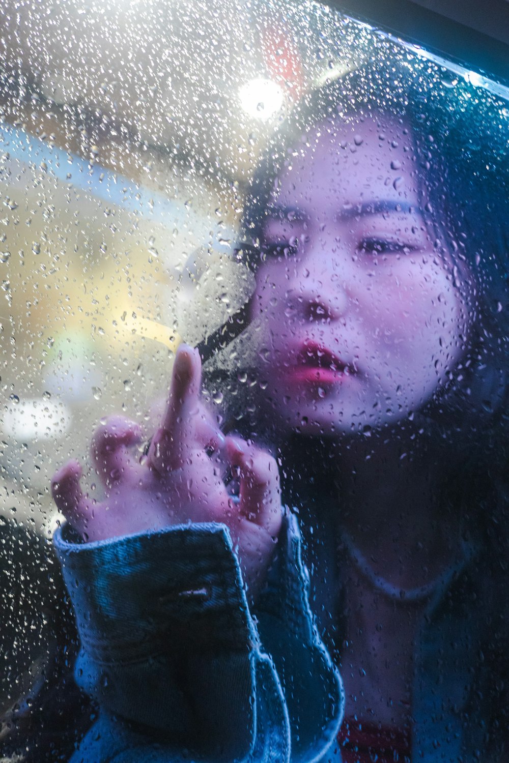 a woman making a peace sign through a rain covered window