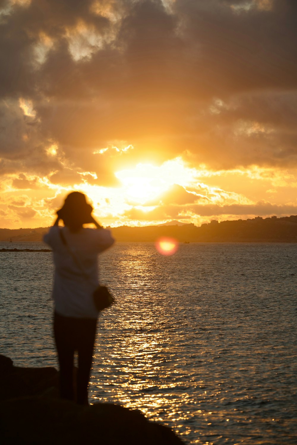 a woman standing on the shore watching the sun set
