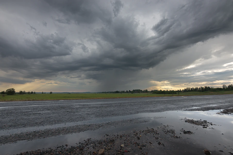 Serene rural landscape under overcast sky with large dark cloud looming on horizon