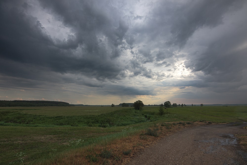 a dirt road in a field under a cloudy sky