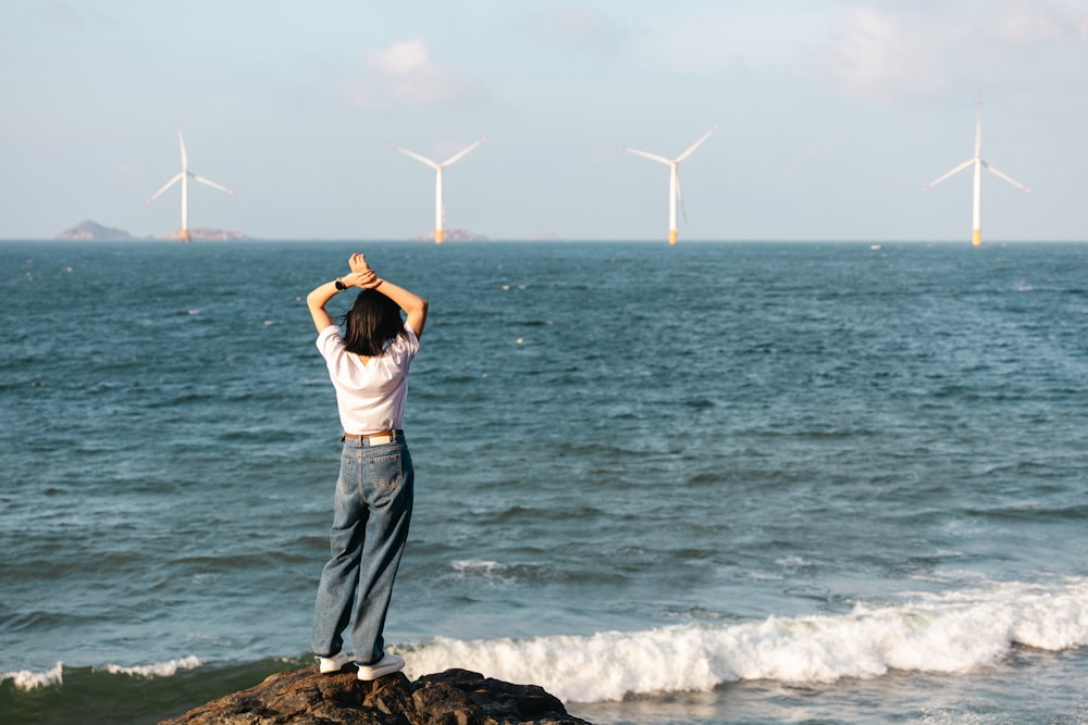 a woman standing on top of a rock near the ocean