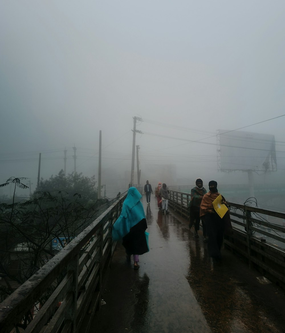 a group of people walking across a bridge on a foggy day