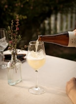 Sprudelnder Kombucha als Sommergetränk im Weinglas mit Eiswürfeln und Blumen im Hintergrund