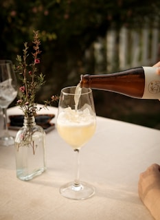 Sprudelnder Kombucha als Sommergetränk im Weinglas mit Eiswürfeln und Blumen im Hintergrund