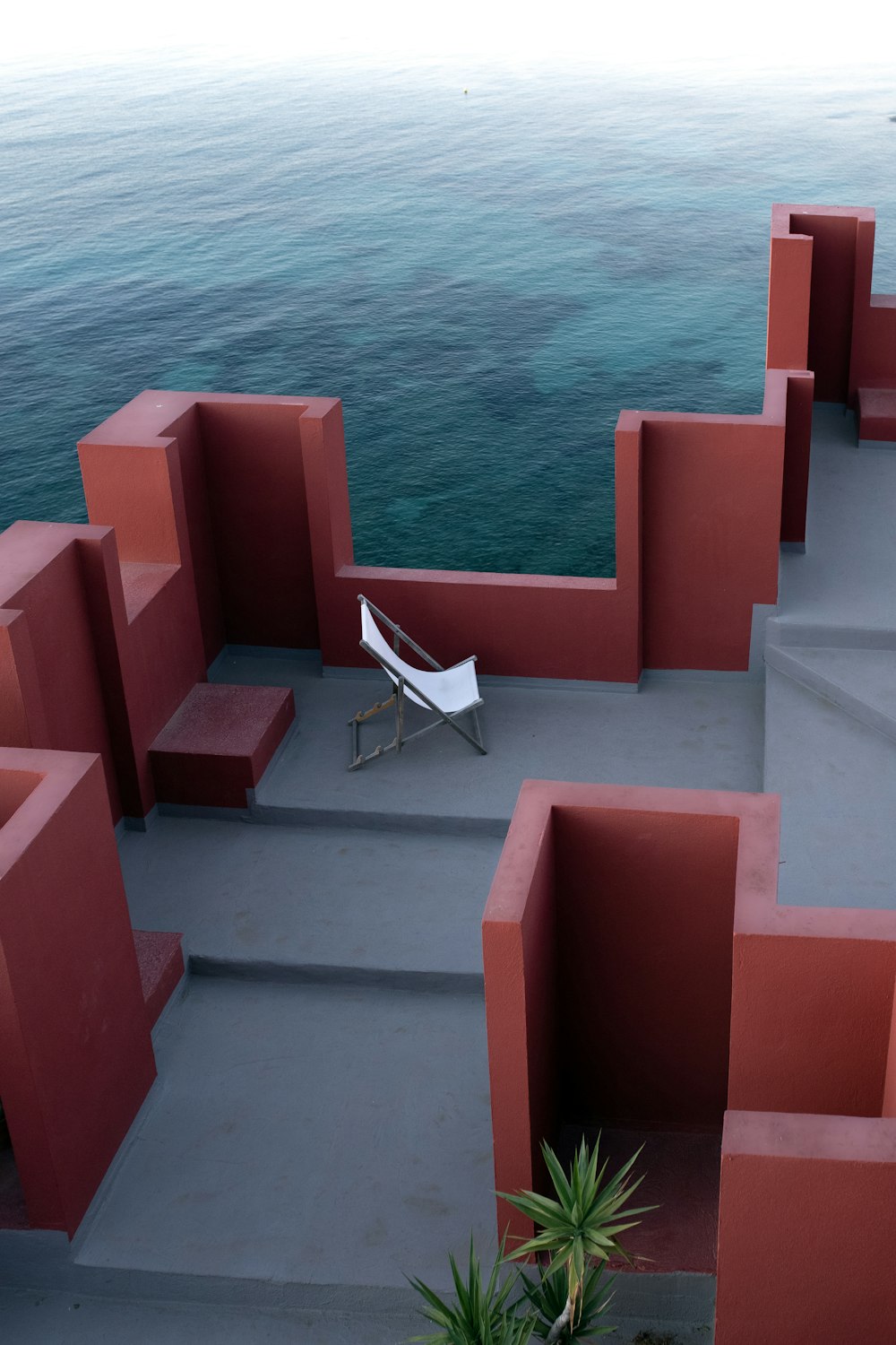 a white chair sitting on top of a cement walkway next to the ocean