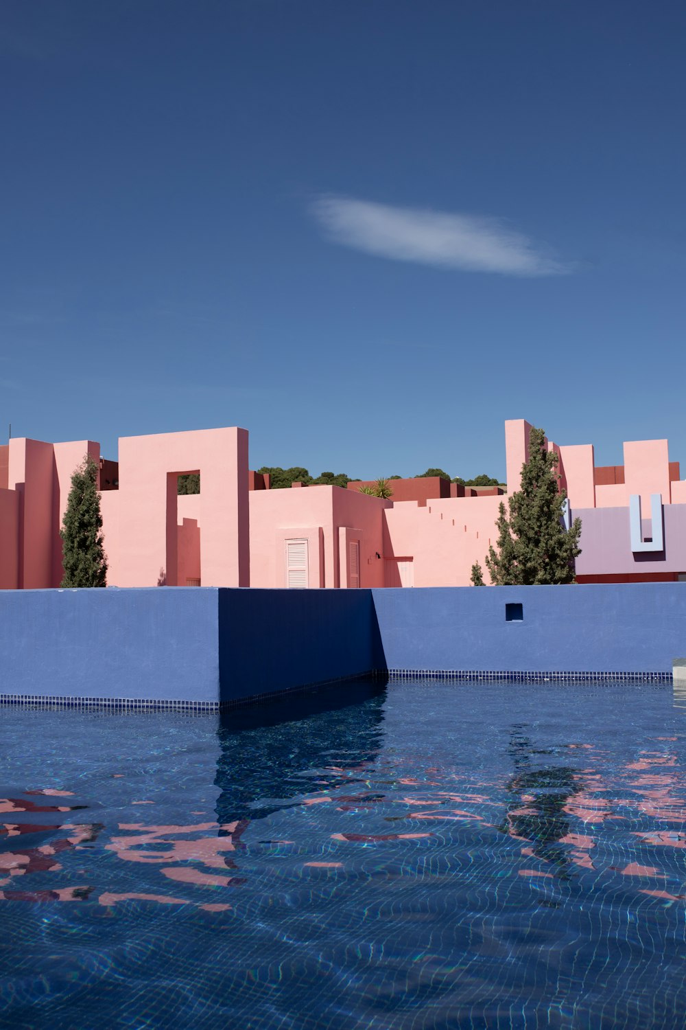 ein blauer Pool mit einem rosafarbenen Gebäude im Hintergrund