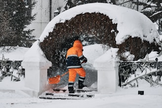 a man in an orange jacket is shoveling snow